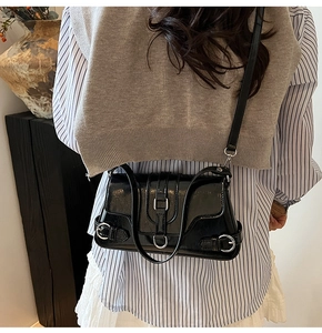 Détail d'un sac d'épaule noir brillant avec boucles argentées porté par un mannequin