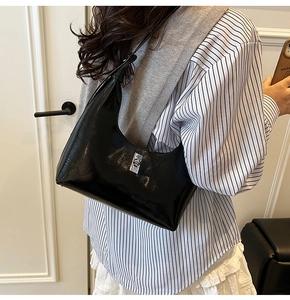 Model wearing a black glossy leather hobo bag with a crescent shape and silver lock
