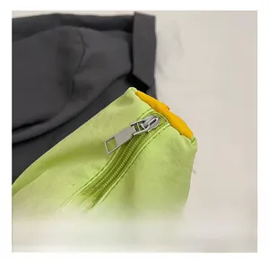 Détail d'une fermeture éclair en métal argenté et d'un passepoil jaune sur un sac vert