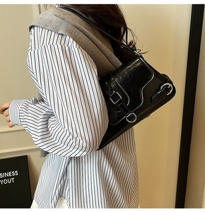 Détail du sac sous le bras en cuir noir brillant avec texture vintage et boucle argentée