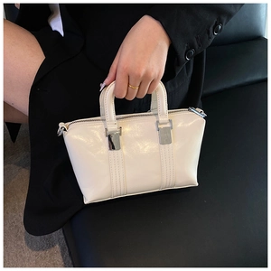 Detail of elegant cream faux leather handbag featuring glossy finish and silver hardware