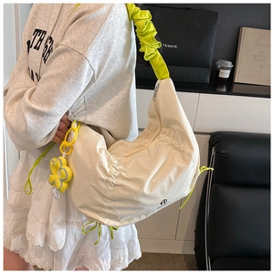 Détail du sac croissant en toile avec bandoulière plissée verte et breloque fleur jaune