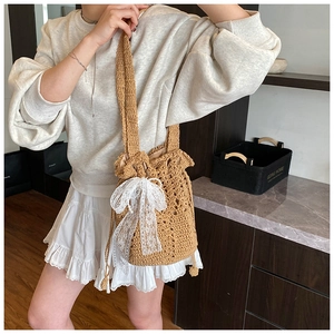 Detail of woven straw bucket bag featuring a large white lace bow and drawstring closure