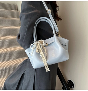Detail der hellblauen Lackledertasche mit Perlenbogen und Spitzenband am Modell