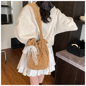 Close-up of hand-woven straw bucket bag with white lace bow and pearl chain detail