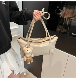 Detail of beige glossy leather shoulder bag with embossed letters and bear pendant