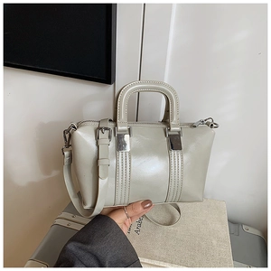 Detail of light grey glossy handbag featuring silver buckles and adjustable strap