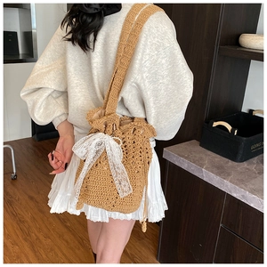 Detail of hand-crocheted bucket bag featuring a large white lace bow and shoulder strap
