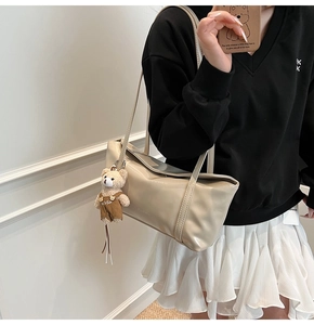 Detail view of large beige tote bag with cute brown bear charm on soft leather surface