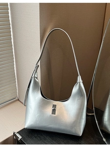 Silver crescent hobo bag with metallic finish and metal turn-lock on a sunlit surface