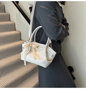 Detail der weißen Handtasche aus glänzendem Leder mit Perlen- und Spitzenanhänger