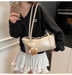 Close-up of the beige shoulder bag's smooth texture and a cute plush bear charm detail