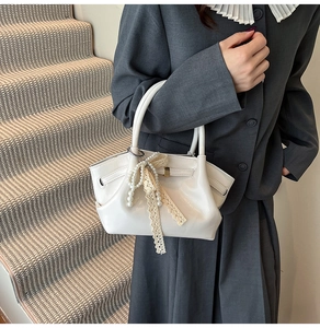 Detail einer weißen Lederhandtasche mit Anhänger aus Perlen und einer Spitzenschleife