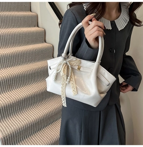 Detailansicht einer weißen Lackledertasche mit Spitzenschleife und Perlenanhängern am Modell