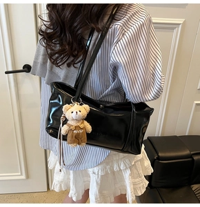 Detail of black patent leather tote bag with a cute plush bear charm on the shoulder strap