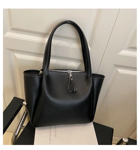Detail of a black leather tote bag featuring contrast white stitching and tassel zippers