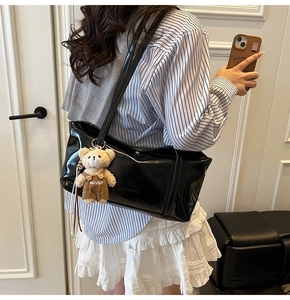 Detail of black glossy tote bag with embossed logo and plush bear charm on the shoulder
