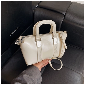 Close-up of cream white patent leather Boston bag with silver hardware on leather sofa