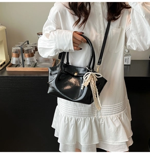 Detail der schwarzen Lackleder-Handtasche mit Perlenspitzen-Anhänger auf Holztisch