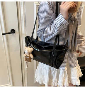 Close-up of black glossy patent leather tote bag with a cute brown plush bear charm accessory