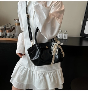 Detail einer schwarzen glänzenden Lederhandtasche mit Perlenanhänger auf weißem Kleid