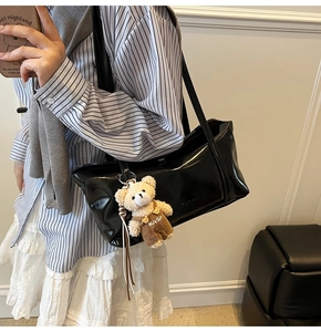 Close-up of a glossy black shoulder bag featuring a cute brown plush bear charm