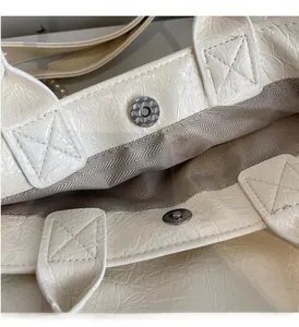 Detail of silver magnetic buckle and herringbone lining on milk white patent tote bag