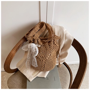 Detail of hand-woven brown straw bucket bag with delicate white lace bow and pearl accent