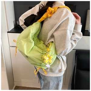 Détail du sac plissé vert avec une bandoulière jaune à cordon et un pendentif fleur