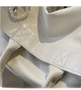 Detail of soft cream faux leather tote featuring pearl handle and metal heart charm
