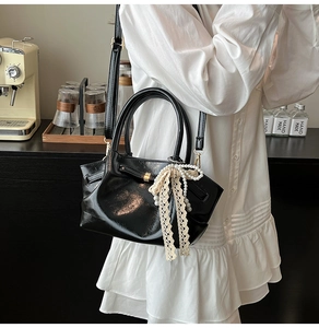 Detail der schwarzen Lackledertasche mit Spitzenschleife und Perlenanhänger am Kleid
