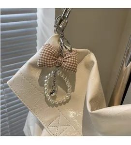 Detail of checkered bow and pearl charm with heart pendant on white leather bag