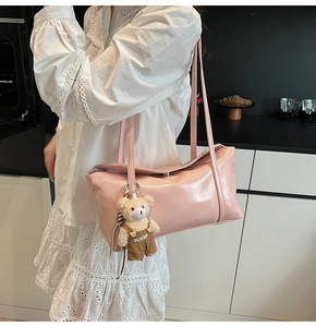 Detailed close-up of a pink patent leather shoulder bag with a plush bear pendant
