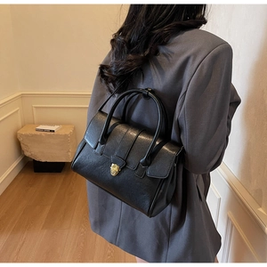 Schwarze matte Handtasche aus Leder mit goldenem Drehverschluss am Model präsentiert