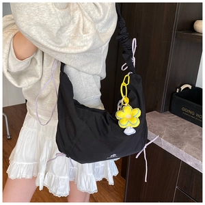 Détail du sac bandoulière noir plissé avec breloque fleur jaune et logo blanc