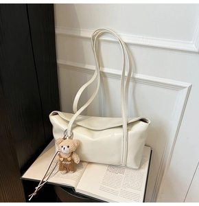 Detail of a creamy white underarm bag with pleated PU leather texture and a cute bear charm