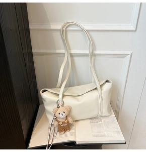 Detail of creamy white leather tote bag with a cute brown teddy bear charm on an open book
