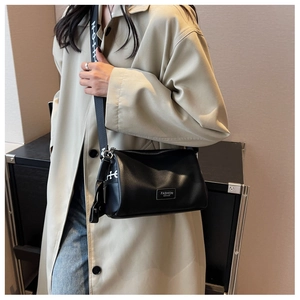 Détail du sac bandoulière en cuir noir texturé avec étiquette mode et sangle large