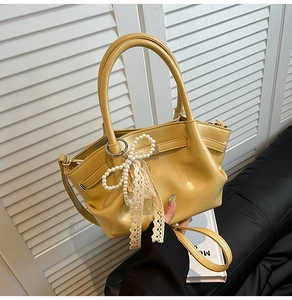 Detail der gelben Ledertasche mit Perlbogen, Spitzenbändern und Faltenstruktur-Design