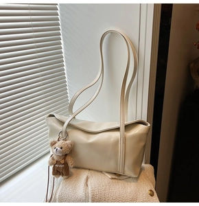 Detail of a creamy white leather baguette bag with a cute teddy bear plush charm