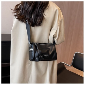 Détail du sac cylindrique en cuir noir avec large bandoulière graphique et fermeture éclair