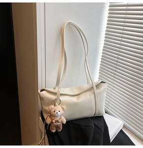 Detailed macro of soft cream PU leather shoulder bag with a cute plush bear pendant