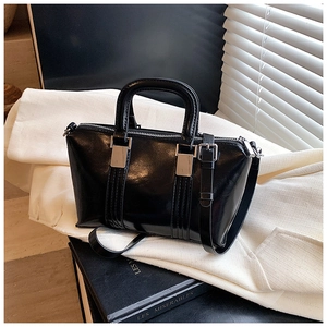 Detail of glossy black Boston handbag with silver hardware and thin leather strap