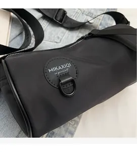 Detail of black oxford cloth cylinder bag featuring brand patch and adjustable nylon strap