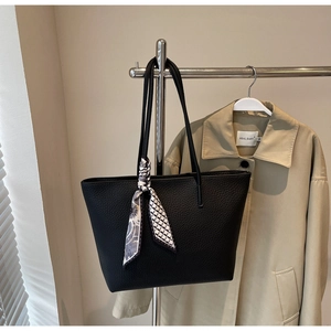 Close-up of black textured leather tote bag with printed silk scarf detail on handle