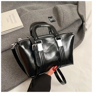 Detail of black patent leather crossbody bag with silver hardware on wool coat