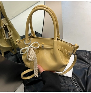 Detail einer cremegelben Plissee-Tasche mit einem Anhänger aus Perlenbogen und Spitze