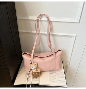 Detailed view of pink shoulder bag with teddy bear pendant on open book