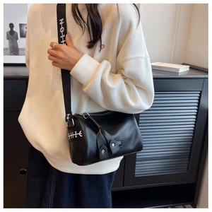 Détail du sac cylindre en cuir noir avec texture grainée et large bandoulière logo