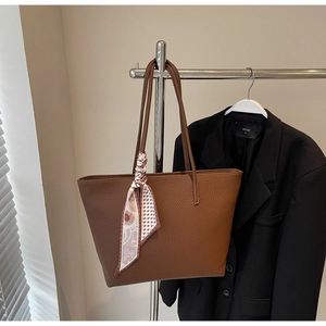 Detail of brown litchi pattern leather tote bag with elegant floral scarf on handle